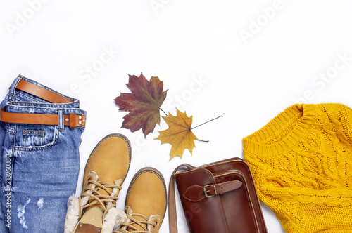 Female orange knitted sweater, blue jeans, leather bag, boots and autumn leaves on white background top view flat lay. Fashion Lady Clothes Set Trendy Cozy Knit Jumper Autumn accessories 