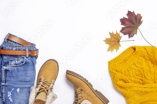 Female orange knitted sweater, blue jeans, boots and autumn leaves on white background top view flat lay. Fashion Lady Clothes Set Trendy Cozy Knit Jumper Autumn accessories Female fashion look