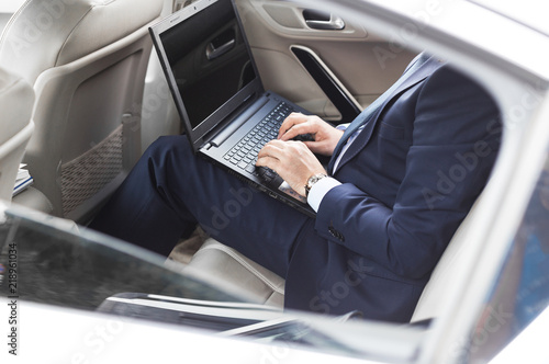 a young business man in a suit is sitting in the back seat of a business car with a laptop and a notebook, business negotiations