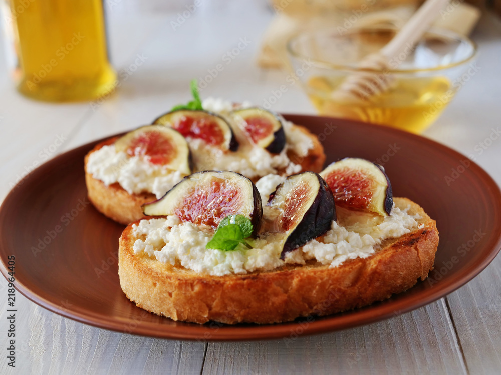Bruschetta toast topped with goat cheese, fig slices, honey and herbs over wooden table