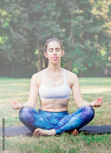 Young woman practicing yoga in nature. Sitting on green grass.