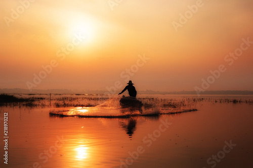 Silhouette of fishermen casting for catching the fish on the wooden boat at the lake in the morning