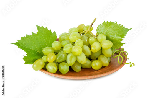 White bunch of ripe grapes with leaves on brown ceramic plate isolated on white background. Berries of grapes in a bunch.