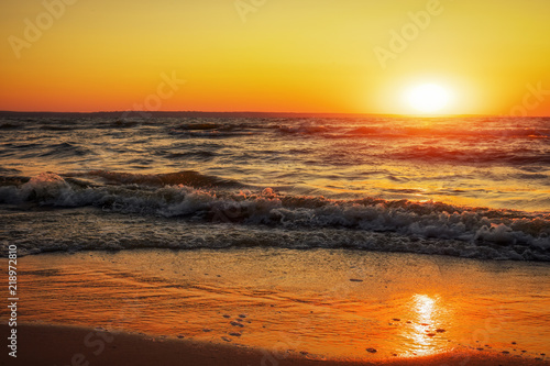 Coast of the sea at dawn. Waves wash the sand. The log lies on the beach. Beautiful time - sunset.