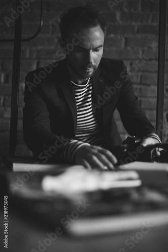 Black and white portrait of handsome stylish man with dark hair and beard in jacket. Man with camera in his hands. Brick wall on background photo