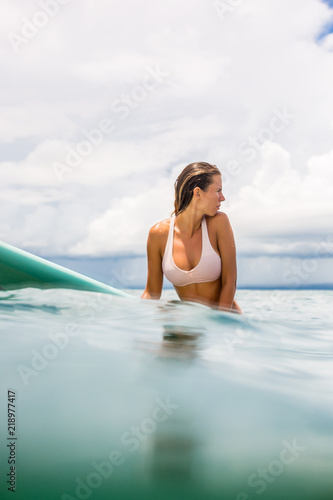Fit beautiful young surfer woman in sexy pink bikini sit on surfing longboard in the open ocean. Modern family lifestyle, people water sport adventure camp and extreme swim on summer vacation.