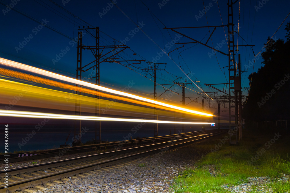 Fototapeta premium An illuminated railroad with light trails of a motion blurred train at dusk, Sochi, Russia 