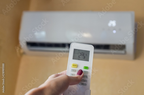 Air conditioner inside the room with woman operating remote controller. / Air conditioner with remote controller