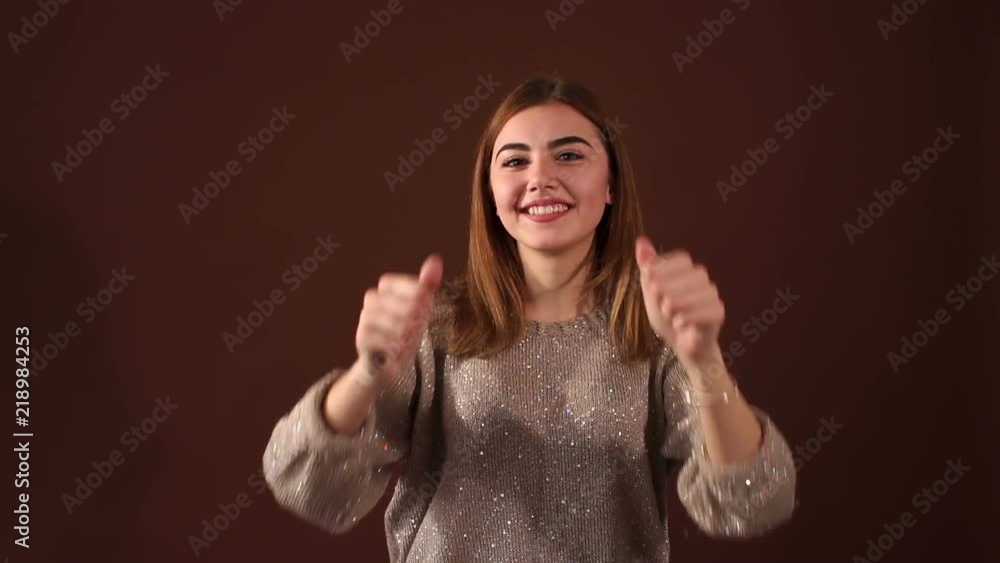 A successful young talented girl shows thumbs up with both hands on a brown background. A successful young talented girl shows thumbs up with both hands on a brown background.