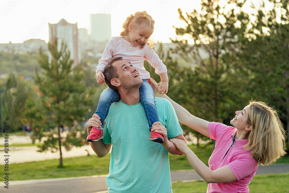 Fototapeta premium active daughter is sitting on his father's neck next mother happy family in the park