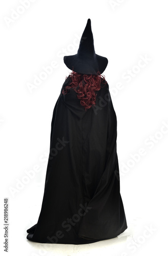 full length portrait of red haired girl wearing long black cloak, pointy hat and witch costume. standing pose, isolated on white studio background. © faestock