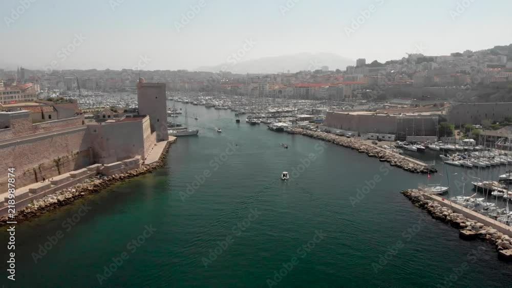 Flying into the old port of Marseille in aerial drone shot. French marina with yachts and boats traveling by historic castle and phare de sainte marie lighthouse into cafetiere. Flying into the old port of Marseille in aerial drone shot. French marina with yachts and boats traveling by historic castle and phare de sainte marie lighthouse into cafetiere.