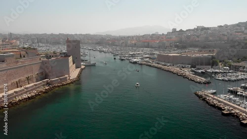 Flying into the old port of Marseille in aerial drone shot. French marina with yachts and boats traveling by historic castle and phare de sainte marie lighthouse into cafetiere.  photo