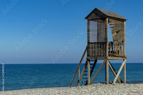 Abandoned rustic wooden lifeguard's tower on shingle beach, blue sky with sea horizon. Lightly rippling waves  © Steve