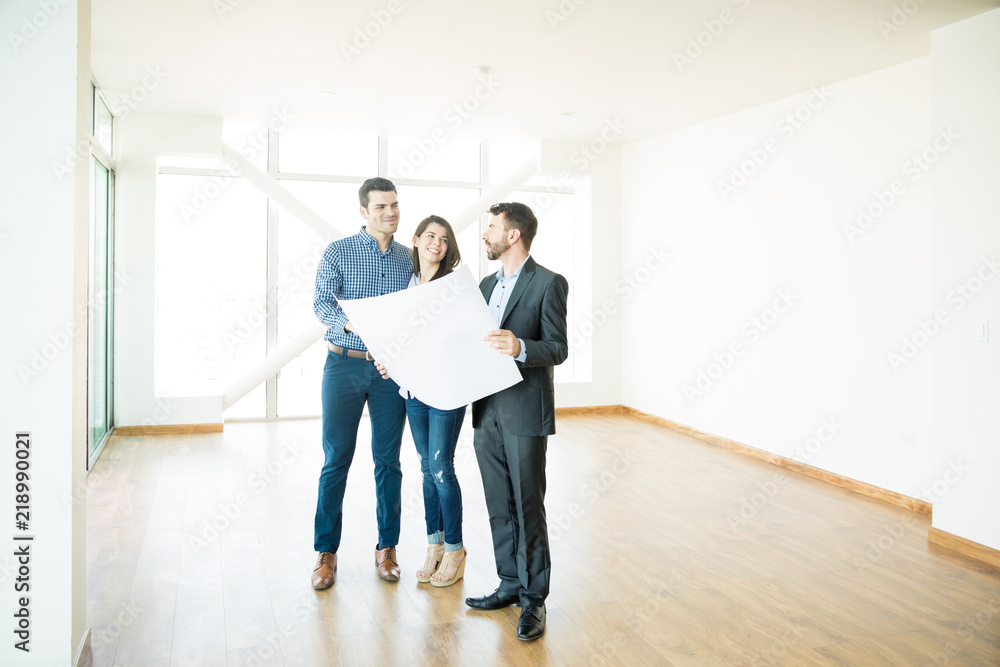 Couple And Estate Agent Discussing Over Blueprint In New Apartment Couple And Estate Agent Discussing Over Blueprint In New Apartment