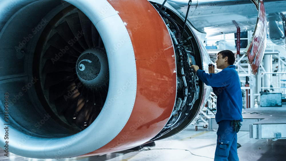 Obraz premium Mechanik obsługi samolotów z lampą błyskową sprawdza silnik samolotu w hangarze.