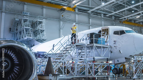 Engineer in Safety Vest Standing next to Airplane in Hangar