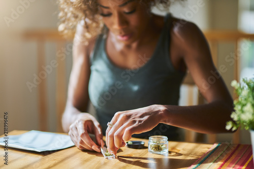 african american woman at home rolling marijuana joint from dispensary bought weed