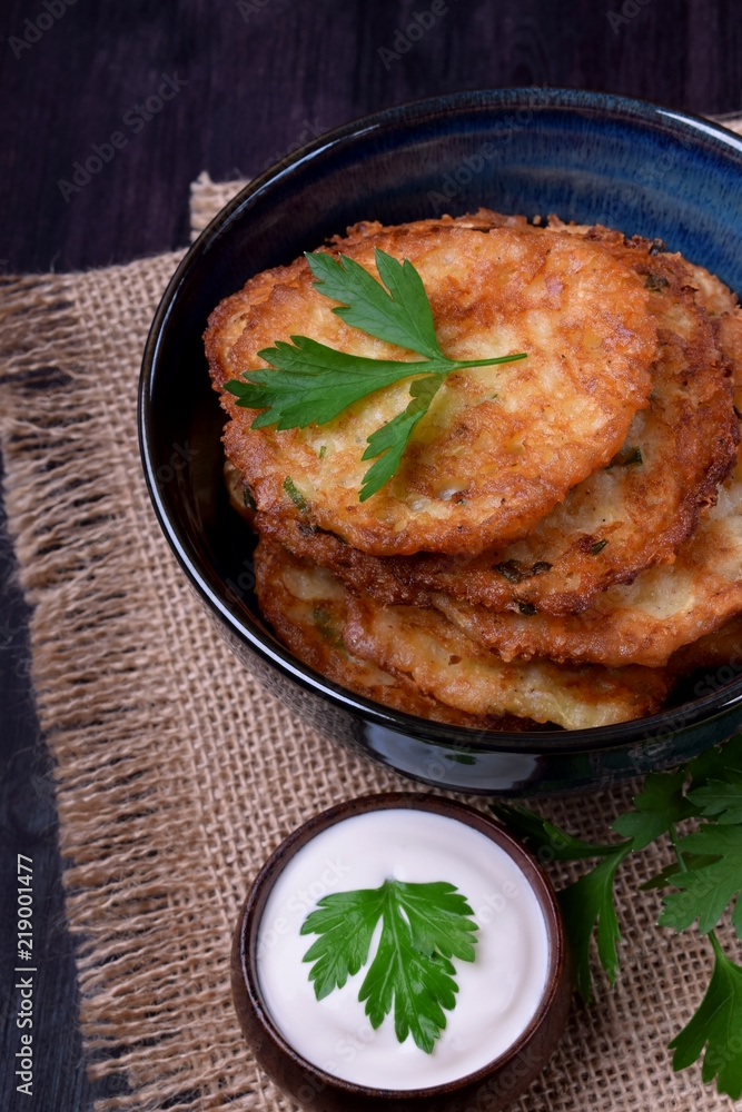 Vegetable pancakes and sour cream topped with parsley leaves on a dark plate Vegetable pancakes and sour cream topped with parsley leaves on a dark plate