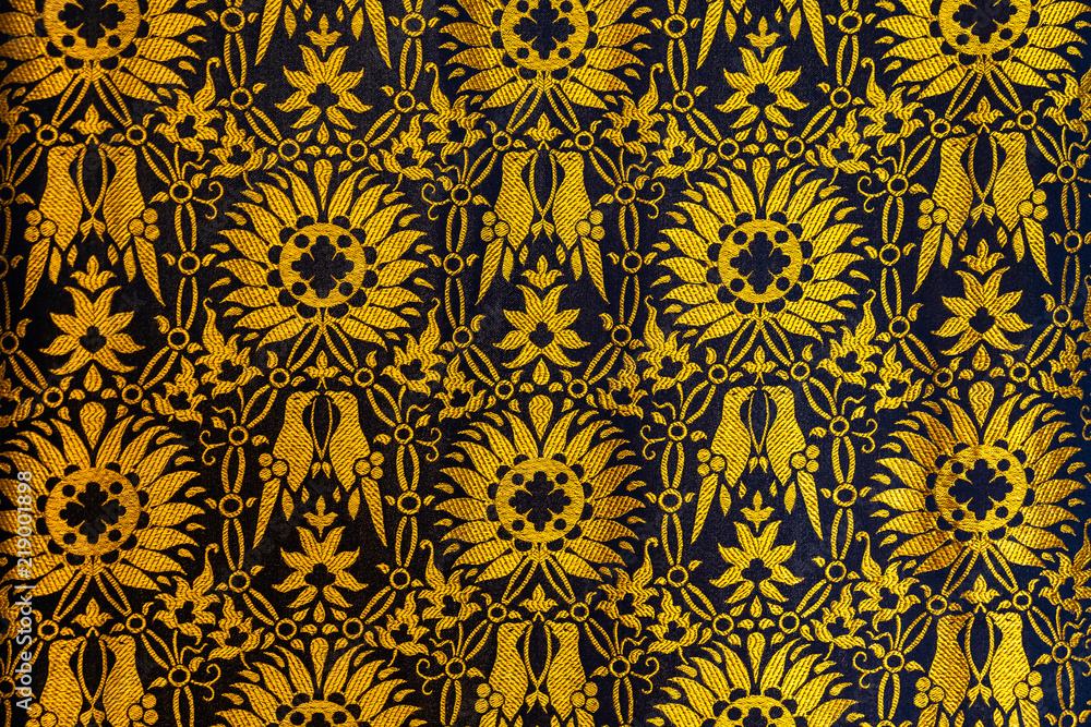 Closeup of a tapestry or fabric patern in gold and black with flowers and birds background backdrop