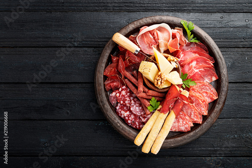 Canvas Print Antipasto platter cold meat with breadsticks, prosciutto, slices ham, beef jerky, salami and cheese platter on wooden board over rustic background