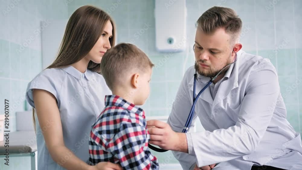 Agitated young mother holding son on knees at pediatrician inspecting in hospital Agitated young mother holding son on knees at pediatrician inspecting in hospital