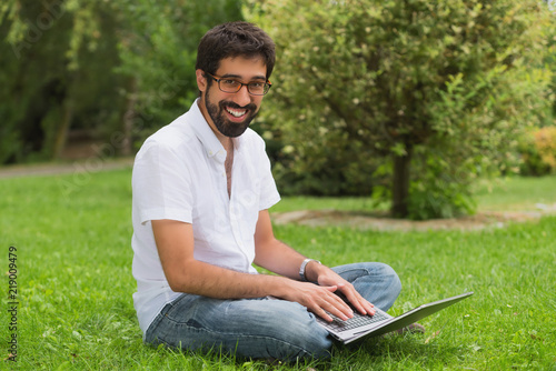 Young man in the park sitting on the grass with a laptop