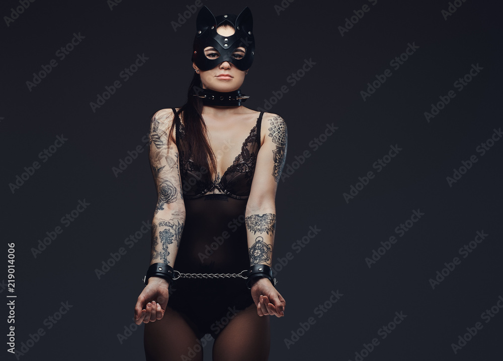 Handcuffed hot brunette mistress girl wearing black lingerie in BDSM cat  leather mask and accessories handcuffed. Isolated on a dark background.  Stock Photo | Adobe Stock