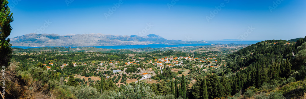 Ultra wide panormaic view of idyllic valley town with red roofs on mediterranean island. Olive groves, cypresses and blue bay in the distance