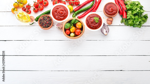 Preparation of tomato sauces and seasonings. Cherry tomatoes, spices, chili peppers. Top view. On a white wooden background. Free copy space.