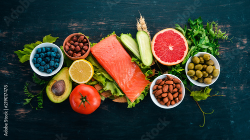 A set of healthy food. Fish, nuts, protein, berries, vegetables and fruits. On a black wooden background. Top view. Free space for text.