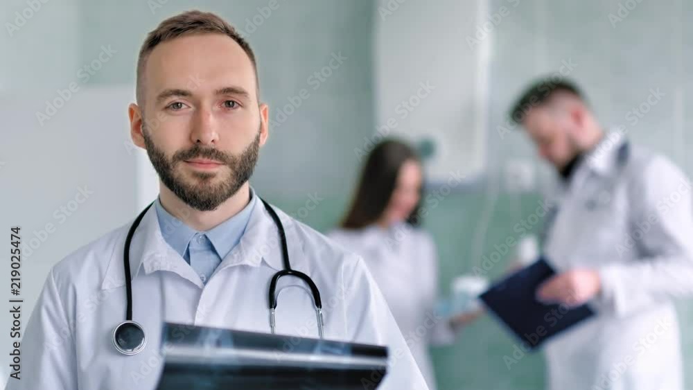 Caucasian male doctor with beard and stethoscope in white lab coat holding X-ray snapshot Caucasian male doctor with beard and stethoscope in white lab coat holding X-ray snapshot