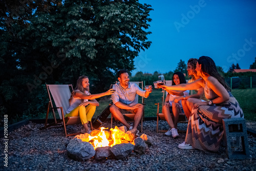 To our great journey! Friends toasting while sitting around firepit. photo