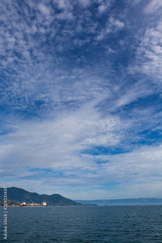 Panoramic view with sea, mountain and blue sky on sunny summer day and a port with ships in Ilha Bela on the coast of São Paulo, Brazil.
