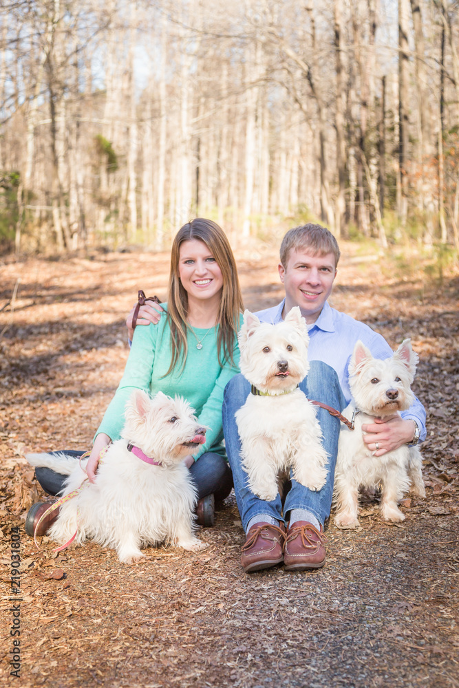 Young Couple with Their Three West Highland White Terriers Outdoors Sitting on the Ground Young Couple with Their Three West Highland White Terriers Outdoors Sitting on the Ground