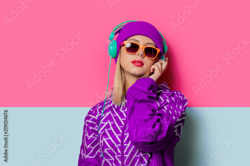 Young blonde girl in 90s sports jacket and hat on pink and blue background. photo