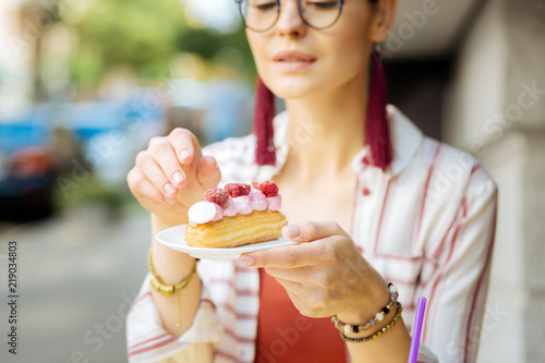 Strawberry dessert. Calm relaxed young woman thoughtfully looking at the tasty raspberry eclair before eating it