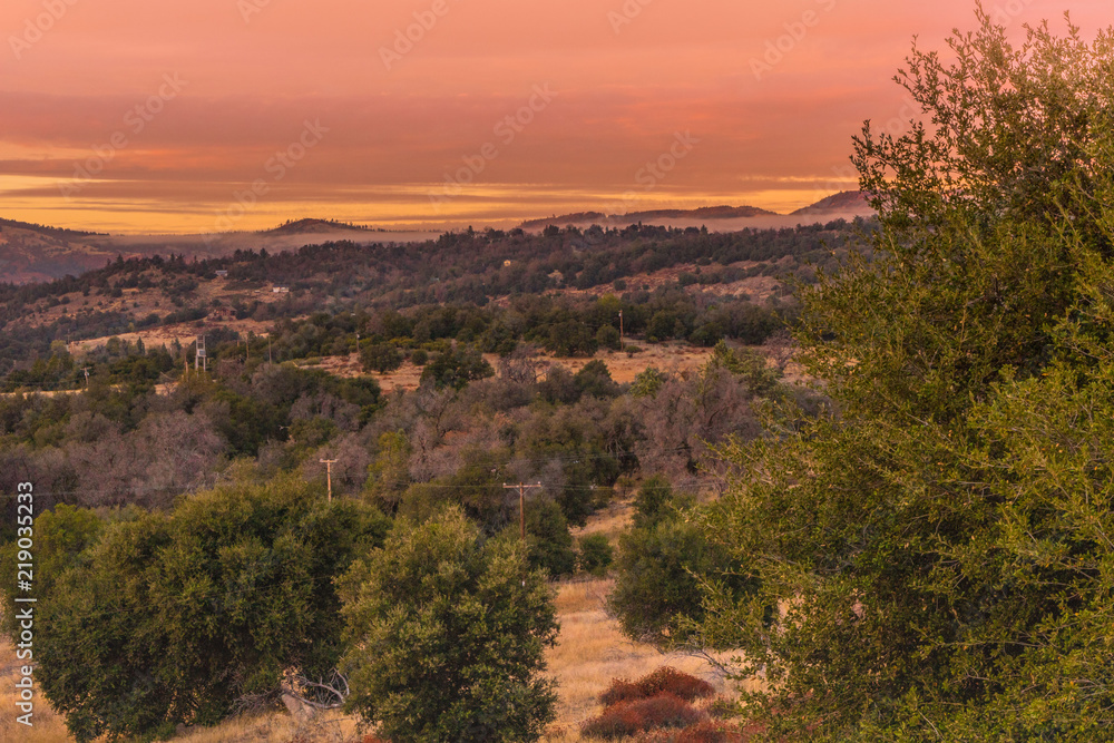 Warm color sunset sky, orange, red, lavender tones, in southern California hills in autumn, oaks in foreground mountains in background