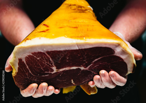 A butcher holds a whole piece of cured meat