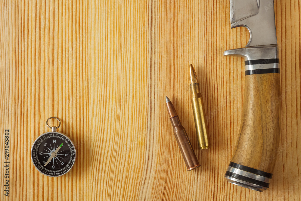 Fototapeta premium Self-made hunting knife, compass and cartridge for a rifle on a wooden background. Close-up