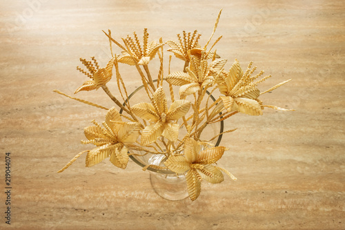 Bouquet of flowers made from straw in a glass vase on a beige background