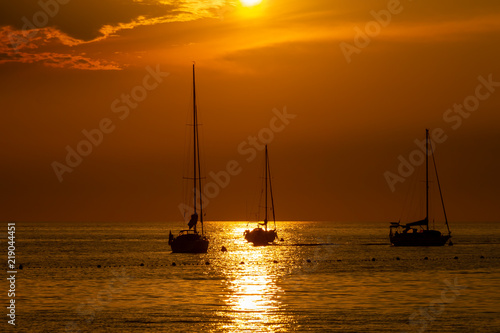 Silhouettes of three anchored sailing boats on the sea during the sunset