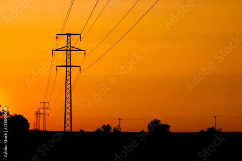 Electricity towers silhouettes on a field during the sunset