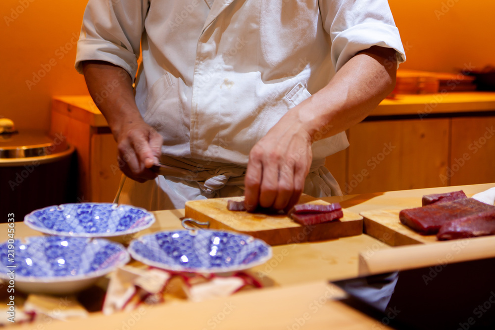 Professional sushi chef using a sharp knife slice fish carefully to make perfect sushi with precision and confident. Dedication and finesse at its best practice to achieve top performance in business