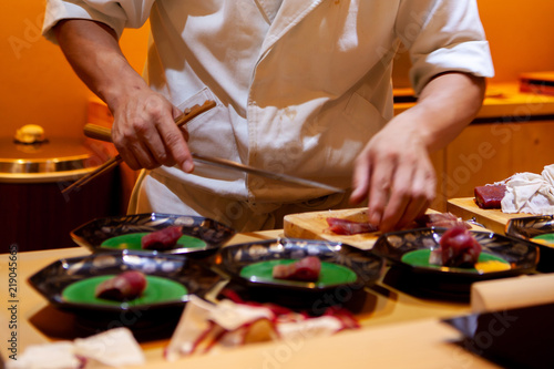 Professional sushi chef using a sharp knife slice fish carefully to make perfect sushi with precision and confident. Dedication and finesse at its best practice to achieve top performance in business