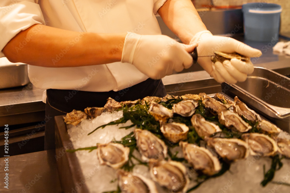Chef shuck fresh oysters with knife. Raw oysters are packed with nutrition, high in calcium, potassium, magnesium, vitamin and mineral. Flavor are sweet and refreshing. Believed to be an aphrodisiac.
