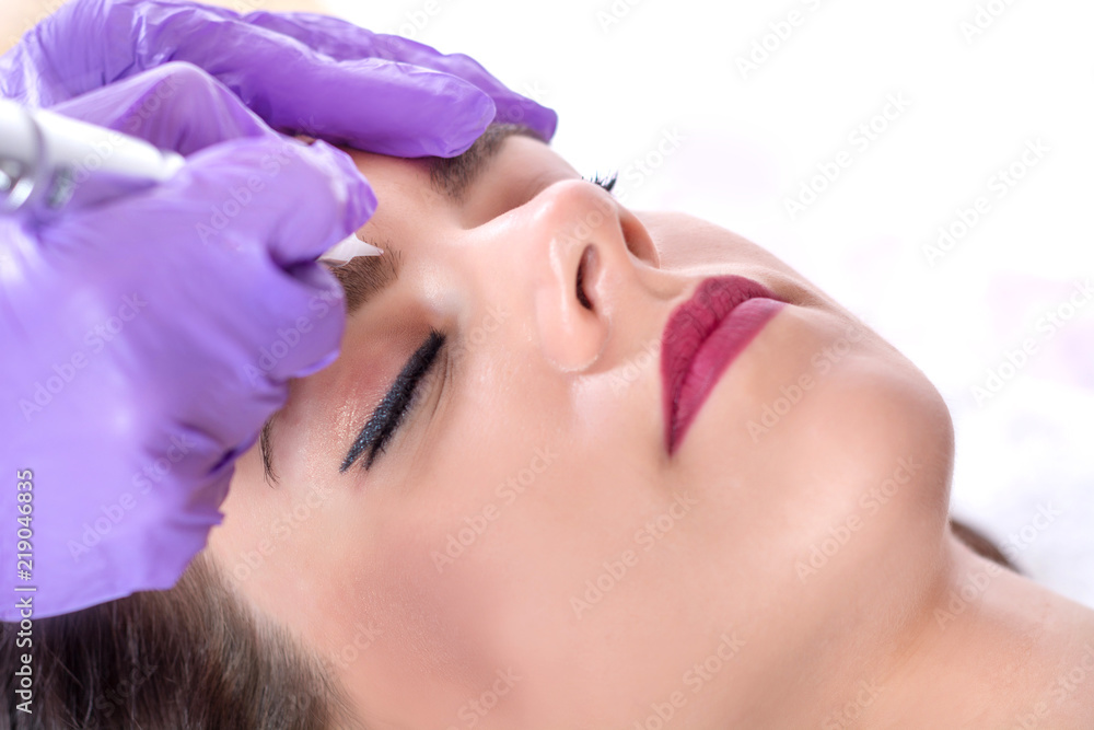 Permanent makeup for eyebrows. Cosmetologist applying tattoo on beautiful women eyebrow. Close up, selective focus
