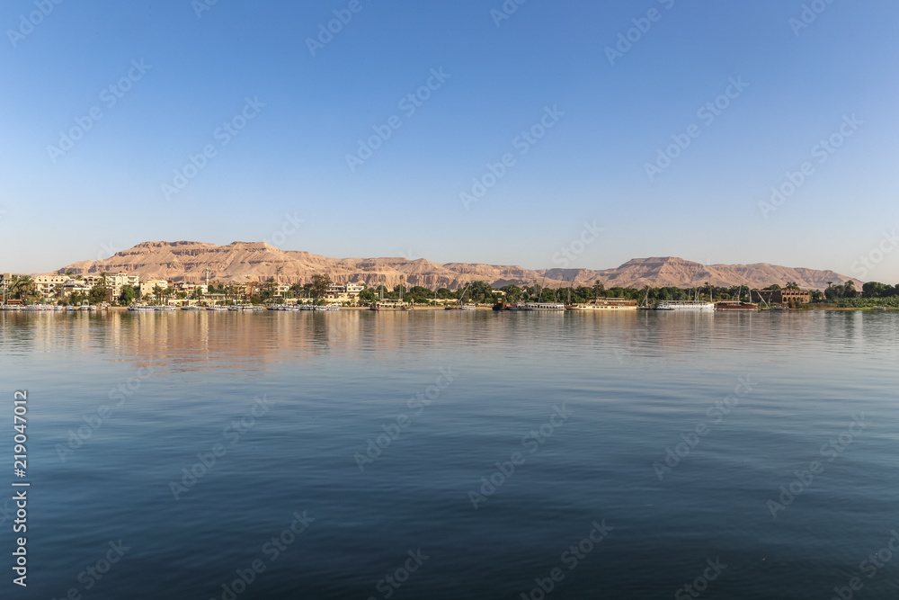 Cityscape from water Nile River with green trees and desert mountain, next to ancient Thebes, in Luxor, Egypt, Africa