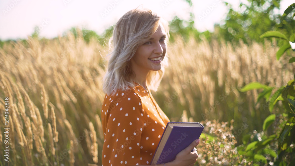 Beautiful happy young woman in field of spikelets and wheat with book on the sunset, blonde in the grass having a good time Beautiful happy young woman in field of spikelets and wheat with book on the sunset, blonde in the grass having a good time