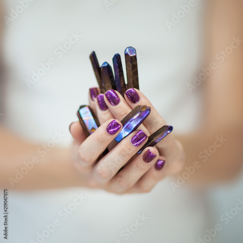 Beautiful woman hands with perfect violet nail polish holding little quartz crystals in purple violet, can be used as background photo